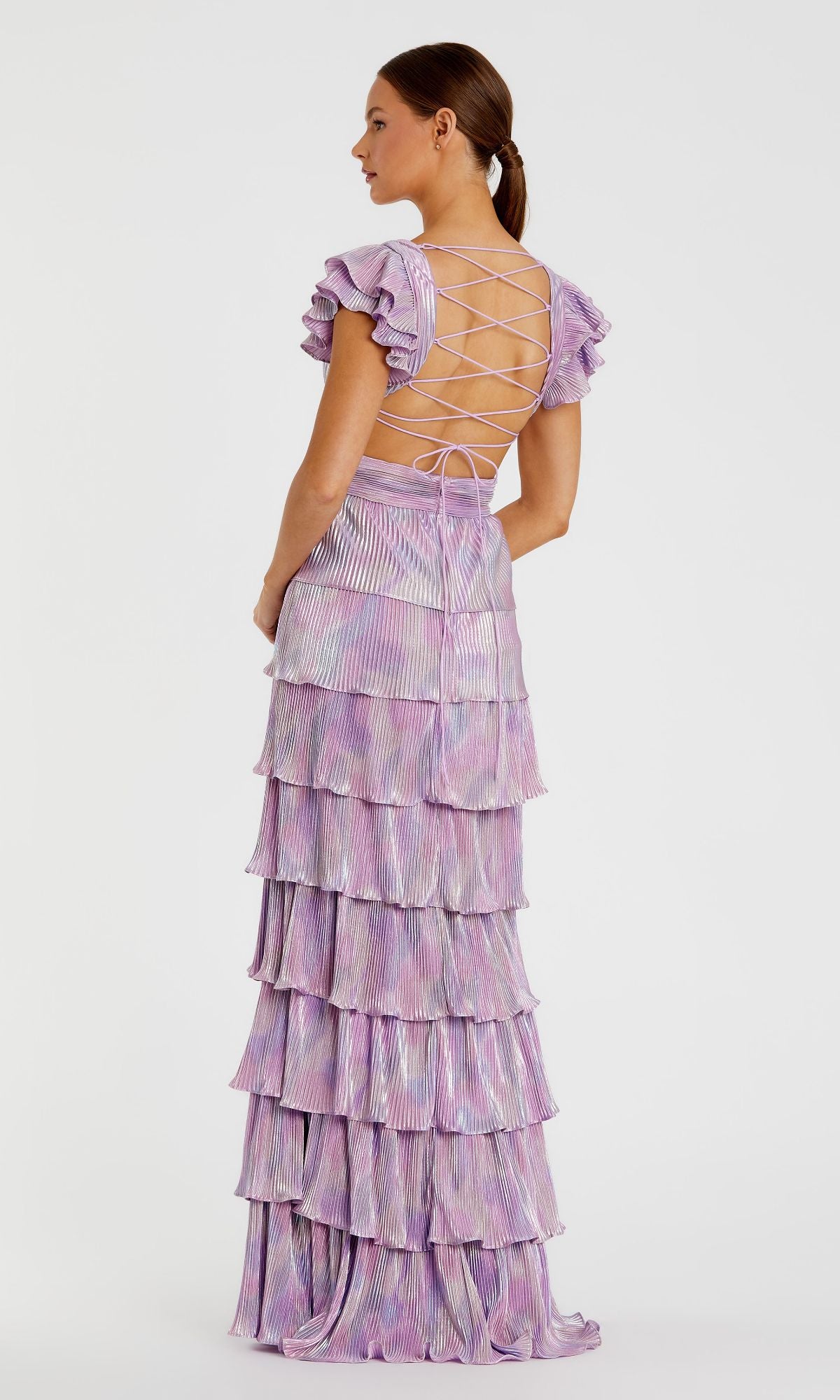 A woman wearing the Mac Duggal Open-Back Tiered Formal Dress 26740, featuring a lavender ruffled maxi skirt and lace-up crisscross open back, stands against a plain white background.